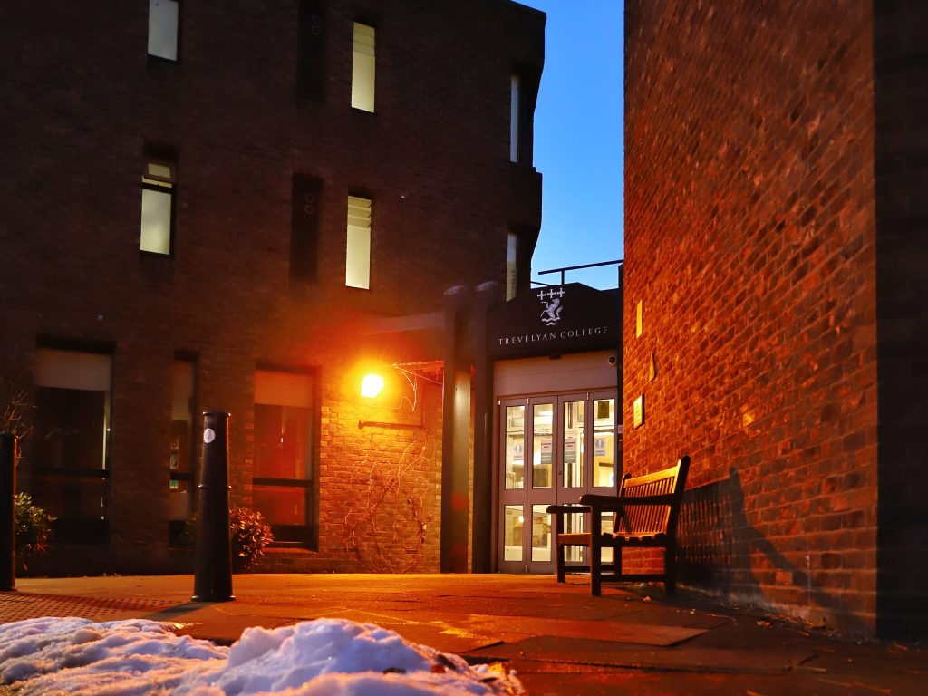An image of the front entrance to Trevs. It is getting dark and the light is glowing; the image colours are quite warm but there is melting snow on the floor.