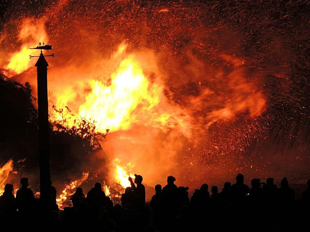 The photo depicts a crowd of people observing a raging forest fire in the distance.