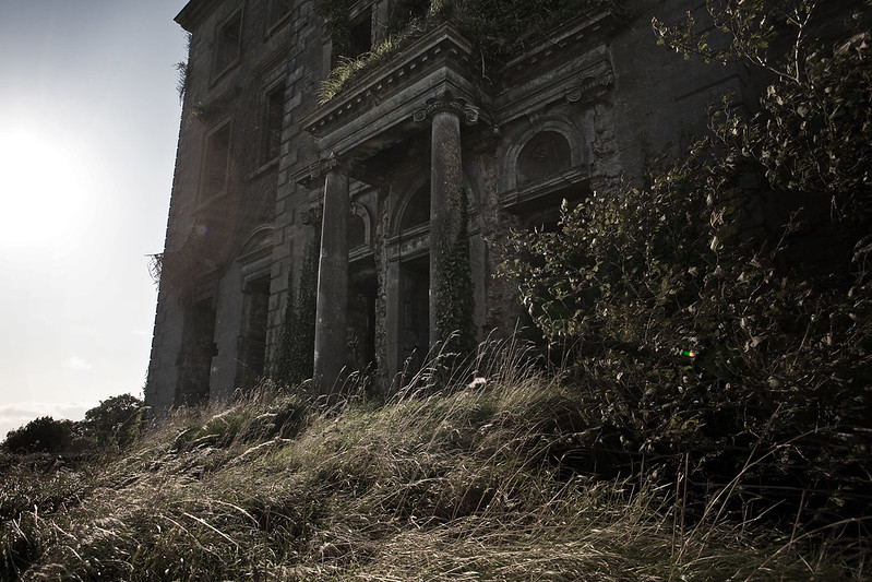 A dark, abandoned manor house with columns and overgrown shrubbery.