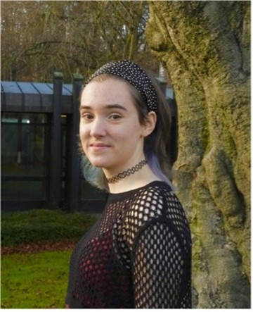 A photo of a lady stood outside trevs, posing by a tree