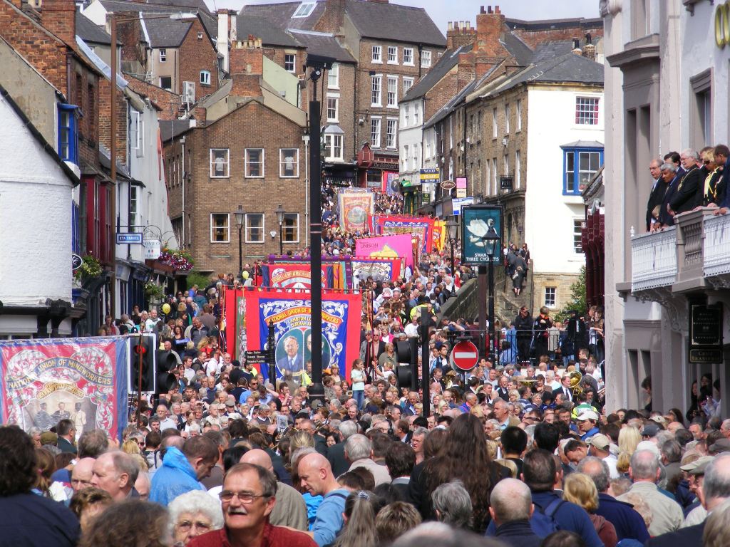 An image of a parade of people coming down Elvet Bridge, carrying a variety of signs supporting the miners. There is so many people that there is little room else.