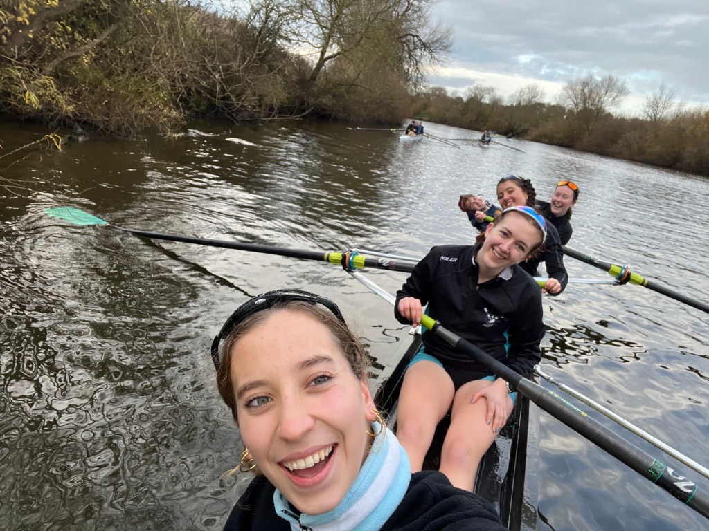 The women's first four posing for the camera whilst in the boat. They are leaning in opposite directions so everyone can be seen.