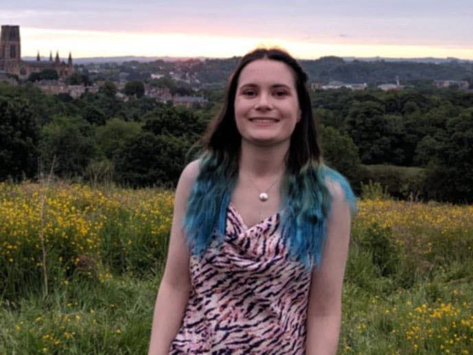 A photo of Immy. She is wearing a formal dress and has black hair which is blue at the bottom. She is stood on top of Observatory Hill at sunrise.