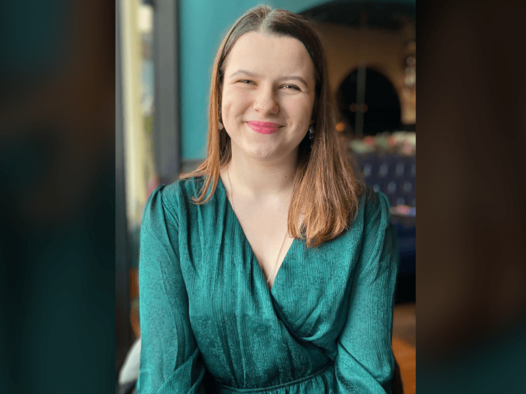 An image of Ollie Laws. They have long hair and are wearing makeup. They are wearing a green dress.