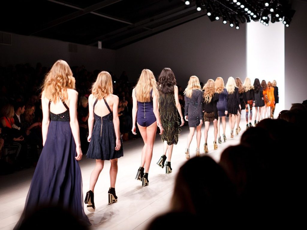 Female models walking on a catwalk wearing formal clothing.