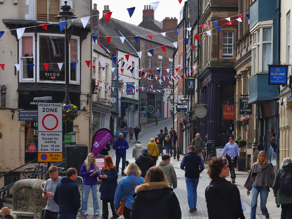 A photograph looking up Saddler Street which is filled with people and has red, white, and blue bunting across the street.