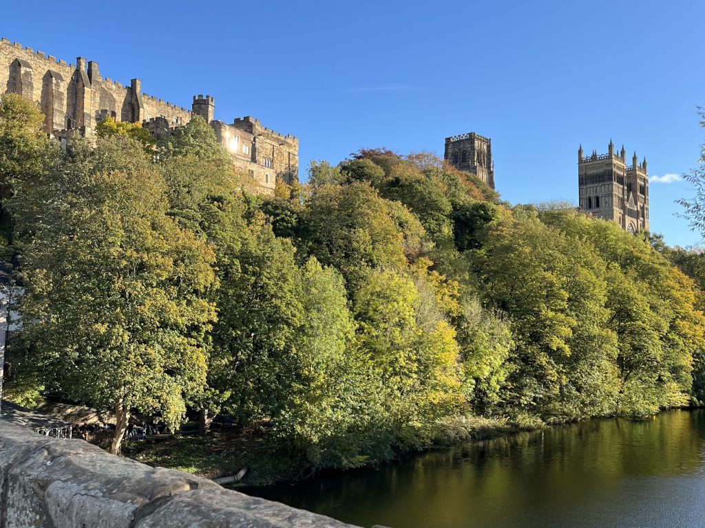 A photograph of Durham Castle and Cathedral taken from Framwellgate Bridge. It's a sunny day with a clear blue sky.