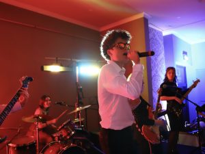 A multicoloured picture of a man wearing sunglasses singing with a band